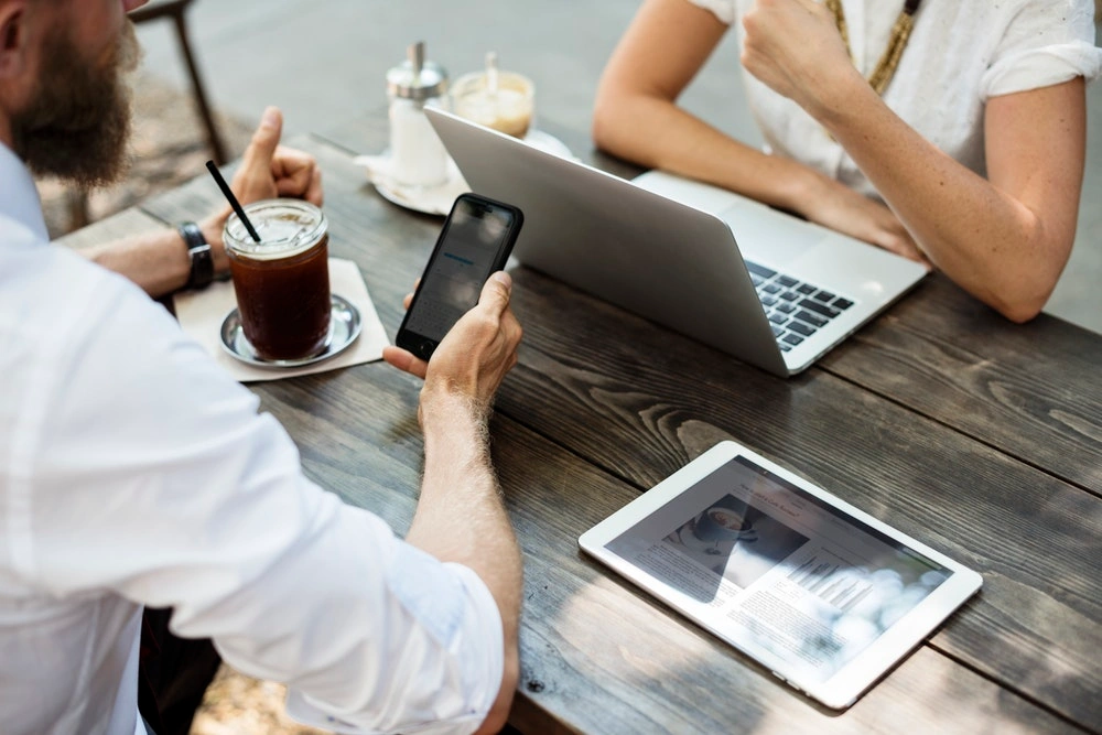 two people at a table, with their electronic devices, having a conversation over coffee