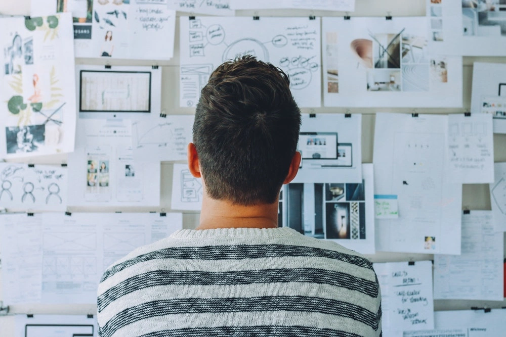 a man looking at a wall full of pictures and papers