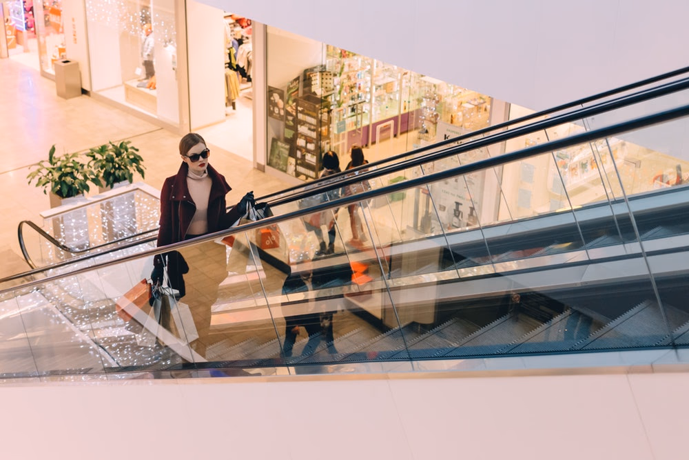 woman with shopping bags riding up the escalator in a mall