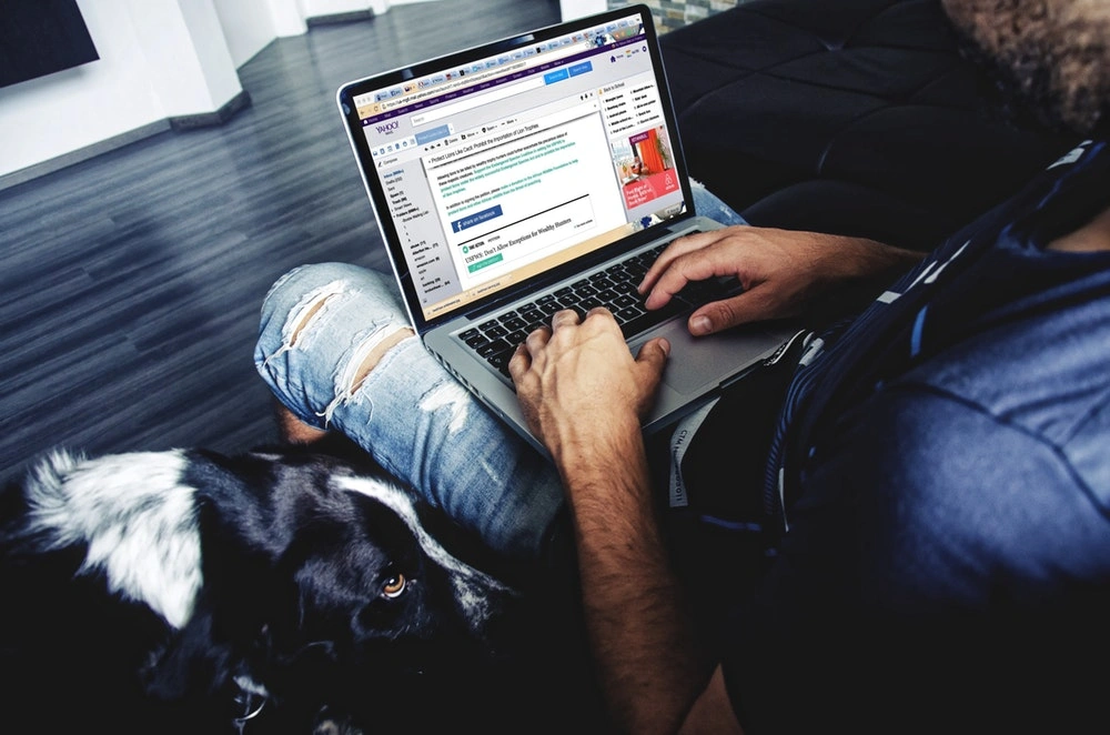 a man sitting with a laptop on his lap, with marketing elements visible on the screen